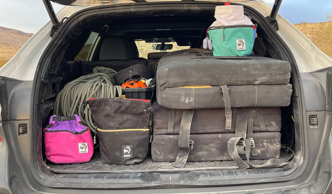 A full bouldering kit loaded in a car trunk — crash pads, rope, and Sesh chalk buckets ready for a session